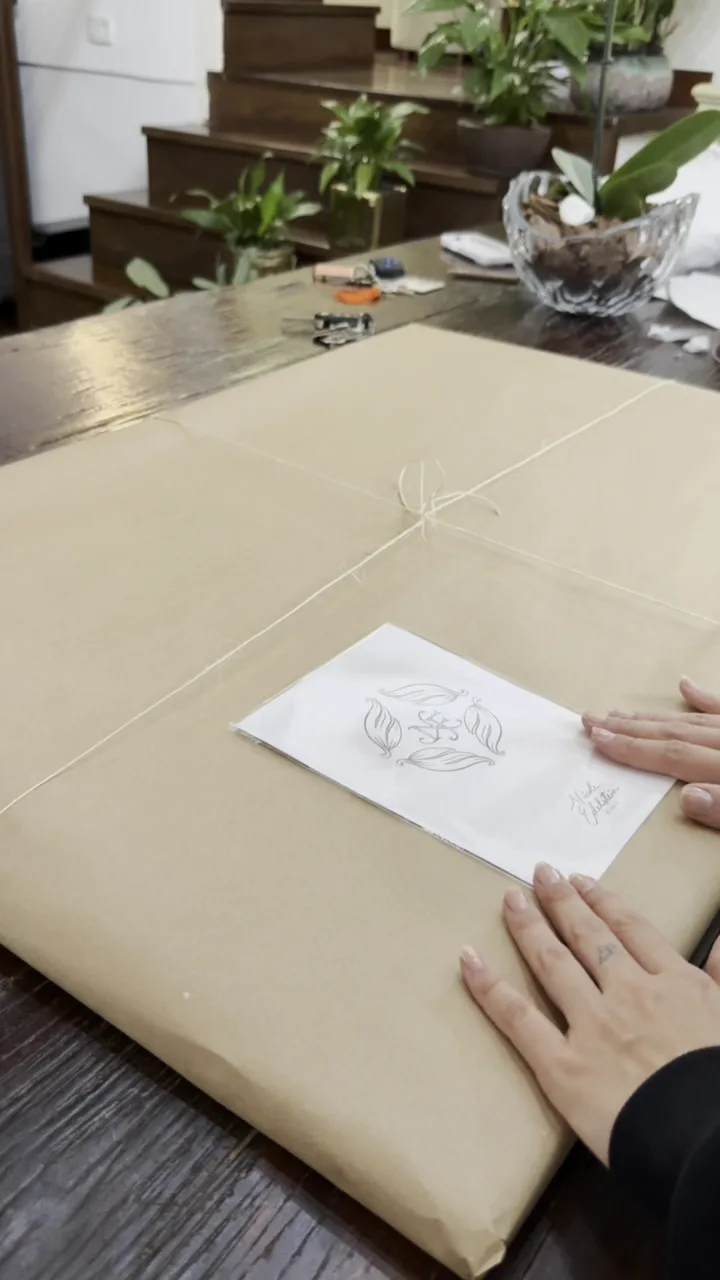 Tela embrulhada em papel kraft com barbante e o selo do monograma
