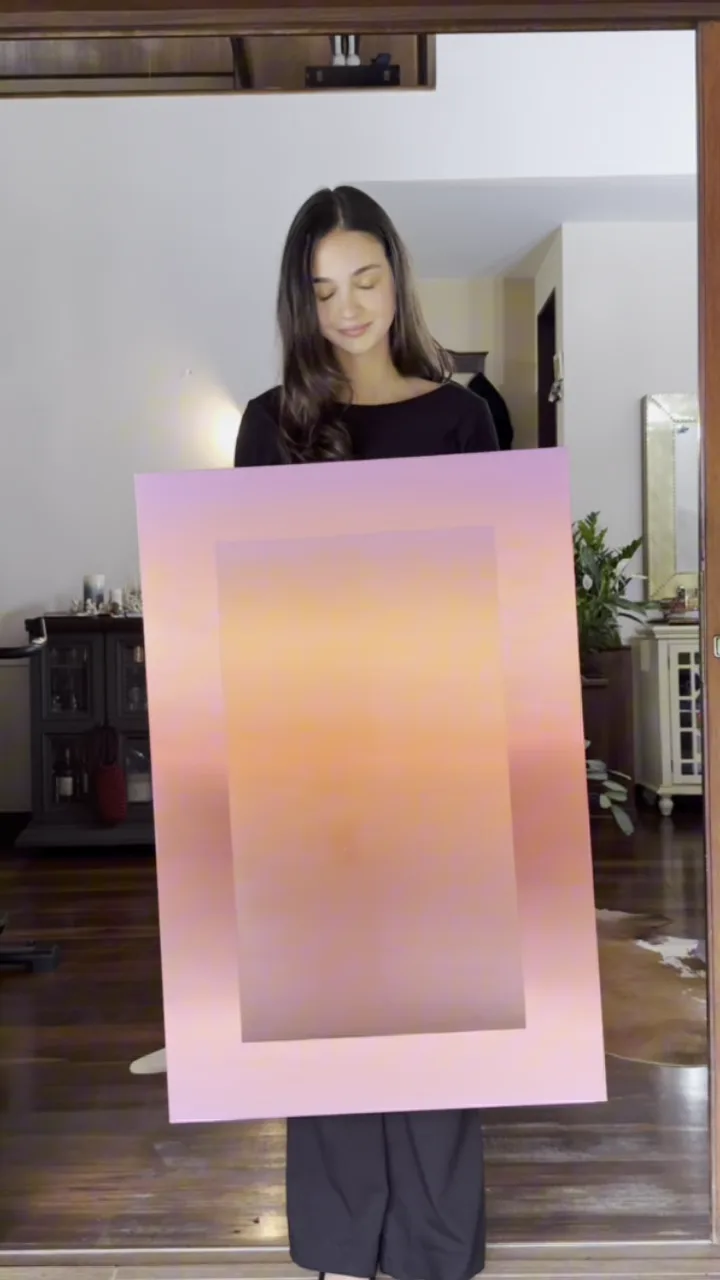 Nicole segurando uma tela em degradê rosa e laranja