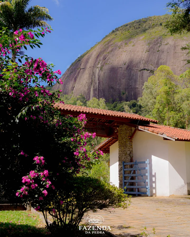 Portaria com buganvílias floridas e a pedra ao fundo