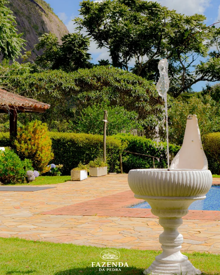 Fonte de água no jardim, com a piscina e a pedra ao fundo