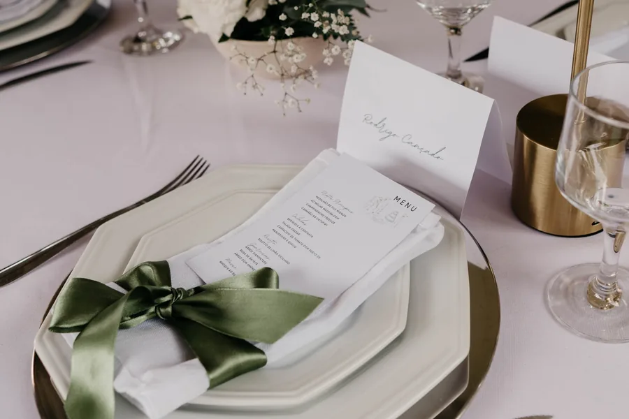Menu ilustrado sobre o guardanapo com laço verde e cartão com o nome do convidado