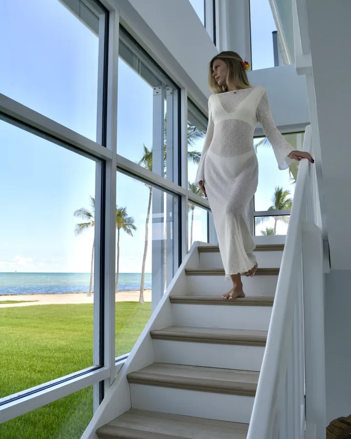Mulher de vestido branco descendo a escada envidraçada da casa