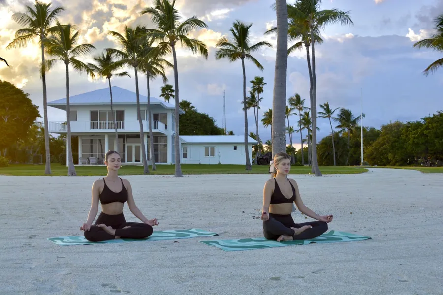 Duas mulheres meditando na areia diante da casa
