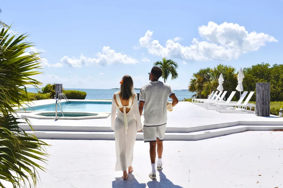 Casal caminhando abraçado ao lado da piscina, de frente para o mar