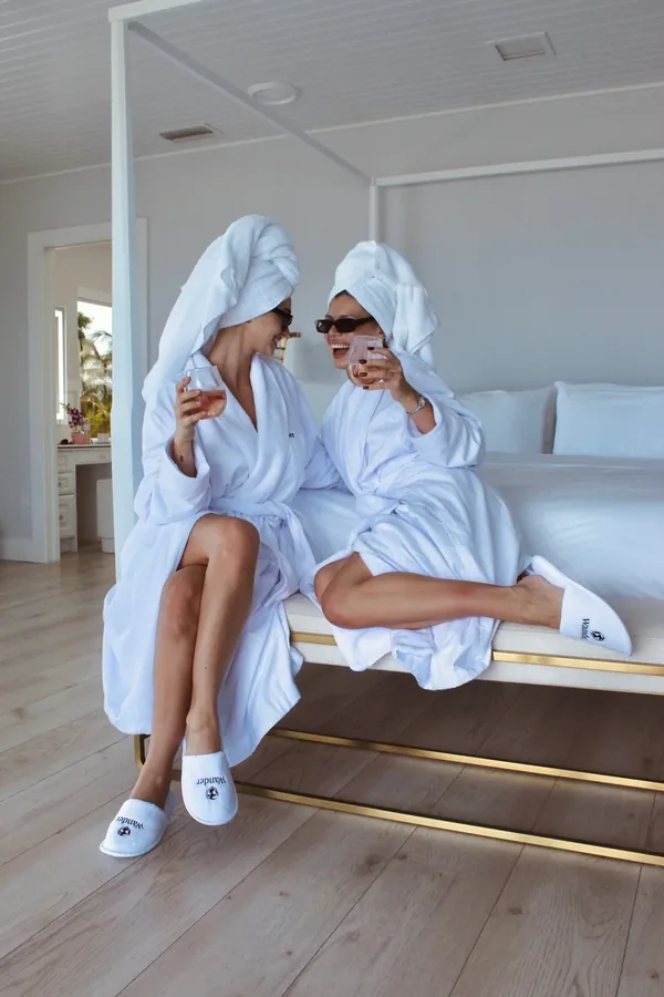 Duas amigas de roupão e toalha na cabeça rindo na cama